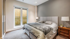 Et soveværelse med en stor seng, et natbord, to sengeborde og en skydedør, der fører ud til en balkon.