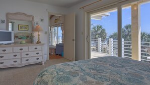 Une chambre dotée d’un grand lit, d’une commode, d’une télévision et d’un balcon offrant une vue sur les palmiers.