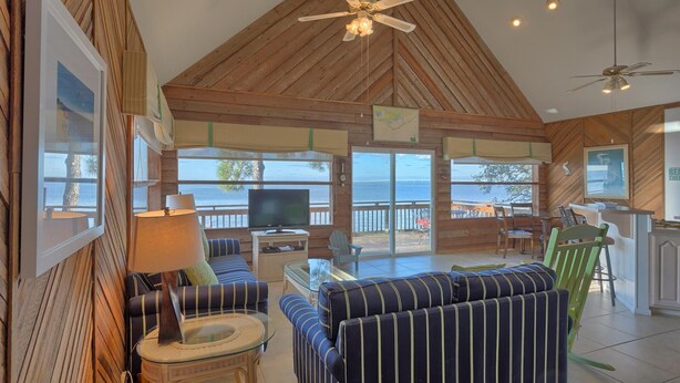 A spacious living area with a large TV, comfortable seating, and a view of the sea. - Welcome to Bienvenue! (St. George Island)