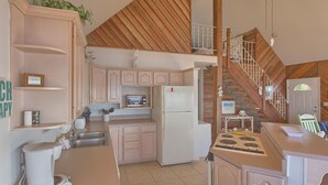 A kitchen with wooden cabinets, a refrigerator, a stove, and a staircase leading to a loft area. - Welcome to Bienvenue! (St. George Island)
