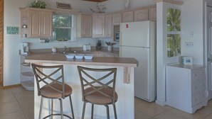 A kitchen with a central island, two bar stools, a refrigerator, and a sink. - Welcome to Bienvenue! (St. George Island)