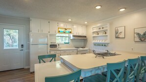 A modern kitchen with white cabinets, a central island with chairs, a built-in oven, and a microwave. - Easy Beach Access - Newly Updated! (St. George Island)