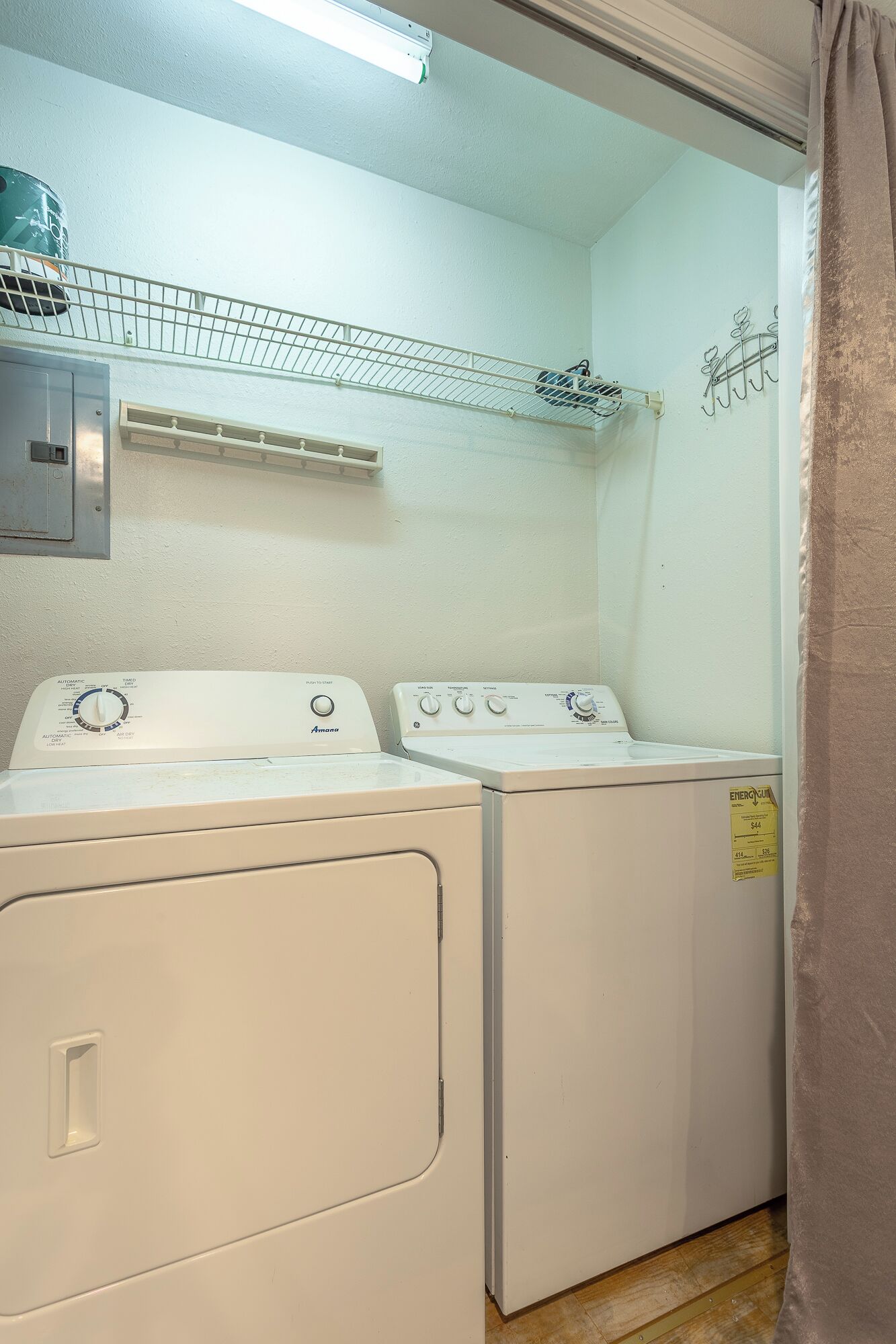 A laundry room with two front-loading washers and dryers, a metal shelf above, and a wall-mounted drying rack.