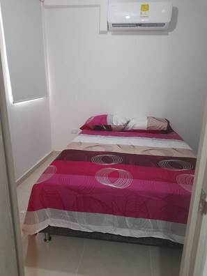 Un dormitorio con una cama, un aire acondicionado blanco y una puerta.