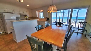 A spacious kitchen with white cabinets, a central island, and a dining area with a wooden table and chairs. - Beachfront! Screen Porch (St. George Island)