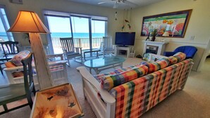 A living room with a sofa, chairs, a glass-top table, a TV, and a fireplace. - Beachfront! Screen Porch (St. George Island)