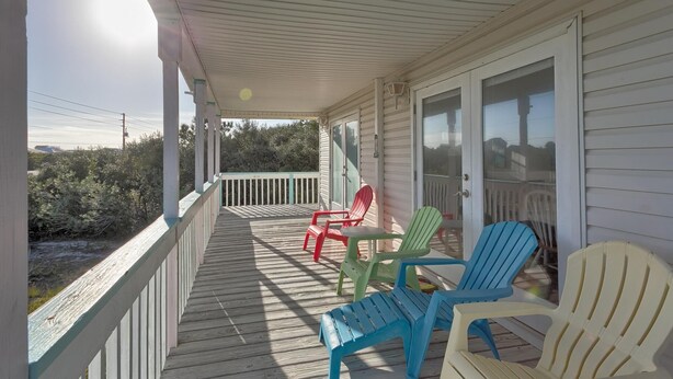 Une véranda couverte avec une terrasse en bois, une porte vitrée et plusieurs fauteuils Adirondack.