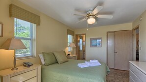 Quarto com cama, abajures, ventilador de teto, penteadeira e porta.