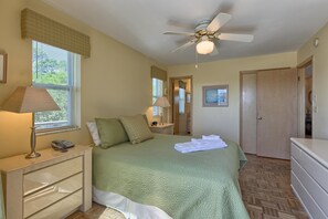 Une chambre Ă coucher avec un lit, des lampes de chevet, un ventilateur de plafond, une commode et une porte.