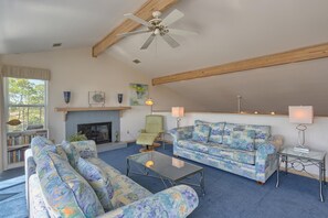 Un salon avec une cheminée, un ventilateur de plafond, un ensemble de canapés et une table basse.