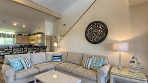 Uma sala de estar moderna com um sofá seccional, uma mesa de centro de vidro e um espaço de jantar com cadeiras e uma mesa.
