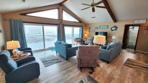 A spacious living room with a large window overlooking the ocean, a ceiling fan, and a cozy seating area with two sofas and a chair. - Beachfront with large sundeck! (St. George Island)