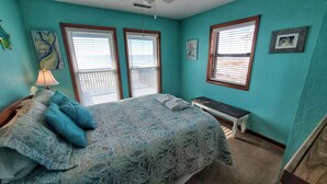 A bedroom with a bed, a bench, and two windows with blinds. - Beachfront with large sundeck! (St. George Island)