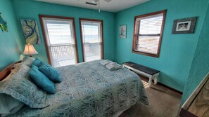 A bedroom with a bed, a bench, and two windows with blinds.