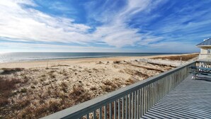 A beach view with a wooden boardwalk leading to a beach area, featuring sandy terrain and sparse vegetation. - Beachfront with large sundeck! (St. George Island)
