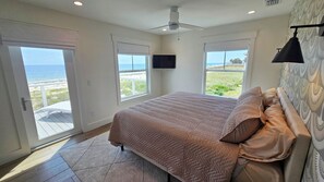 Relax in this serene bedroom with a large bed, ceiling fan, and flat-screen TV, plus a window offering a view of the beach.