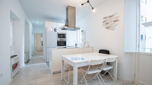 A modern kitchen with white cabinetry, a central island, and a dining area with a white table and chairs. - Apartment Las Lectoras de Cadiz (Cádiz)