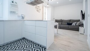 A modern kitchen with white cabinets, a patterned floor, and a grey sofa in the living area. - Apartment Las Lectoras de Cadiz (Cádiz)