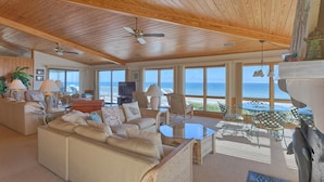 A spacious living room with a high ceiling, large windows offering ocean views, a comfortable sofa, and a glass coffee table. - Welcome to Sea Knight! (St. George Island)