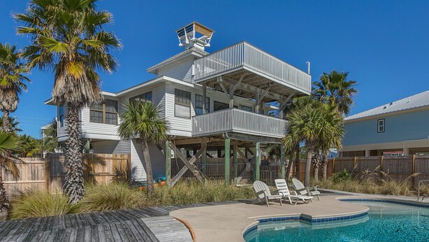 Une maison à deux étages avec une piscine, une terrasse en bois et des palmiers.