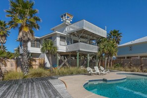 Une maison à deux étages avec une piscine, une terrasse en bois et des palmiers.
