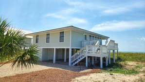 Een twee verdiepingen tellend strandhuis met een overdekte veranda en een trap naar een balkon.