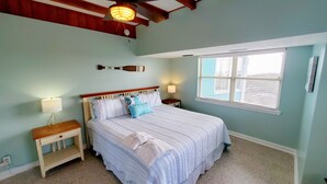 Ein Schlafzimmer mit einem Bett, Nachttischen, einem Fenster und einer Deckenleuchte.