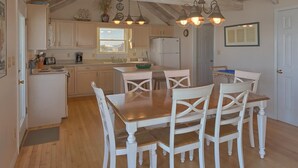 A kitchen with wooden cabinets, a dining table with white chairs, and pendant lights. - Beachfront! Large sundeck with screened in porch! (St. George Island)