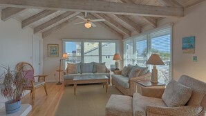 A spacious living room with a high ceiling, wicker furniture, and large windows. - Beachfront! Large sundeck with screened in porch! (St. George Island)