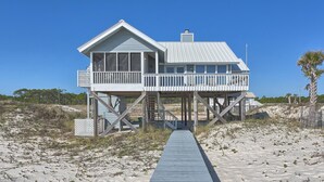 A beachfront house with a wooden deck and a balcony, surrounded by sand and sparse vegetation. - Beachfront! Large sundeck with screened in porch! (St. George Island)