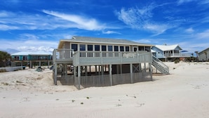 Een strandhuis met een balkon en een overdekt terras, gelegen op zand.