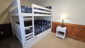 Uma cama de beliche com colcha temática náutica, uma mesa de cabeceira com abajur e um painel de parede de madeira.