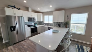 Una cocina moderna con armarios blancos, electrodomésticos de acero inoxidable, una isla grande y vistas al exterior.