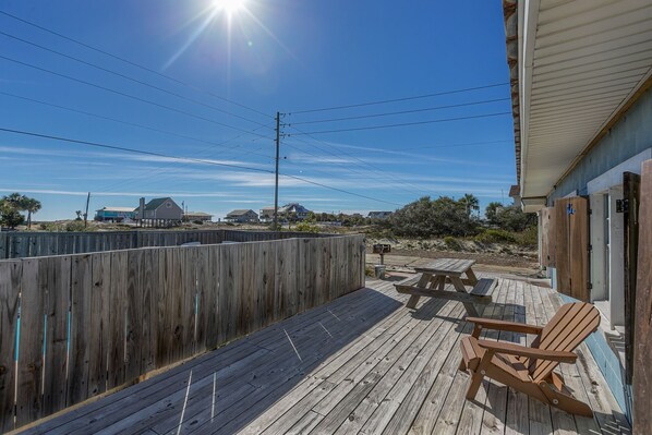 Une terrasse en bois avec une chaise en bois, une table de pique-nique et, en arrière-plan, une vue sur des maisons et la plage.