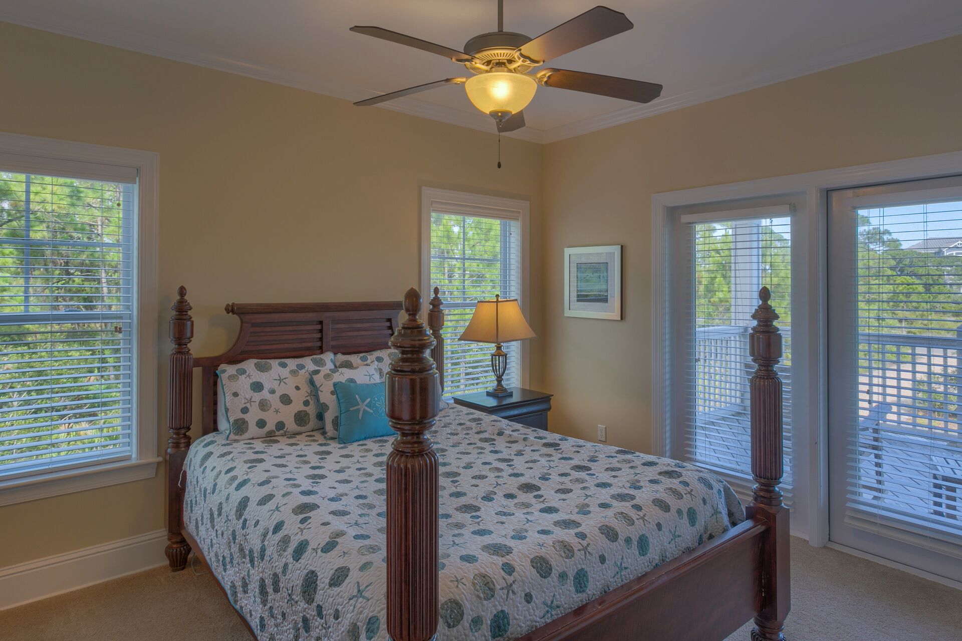 A bedroom with a four-poster bed, a ceiling fan, and large windows with blinds.
