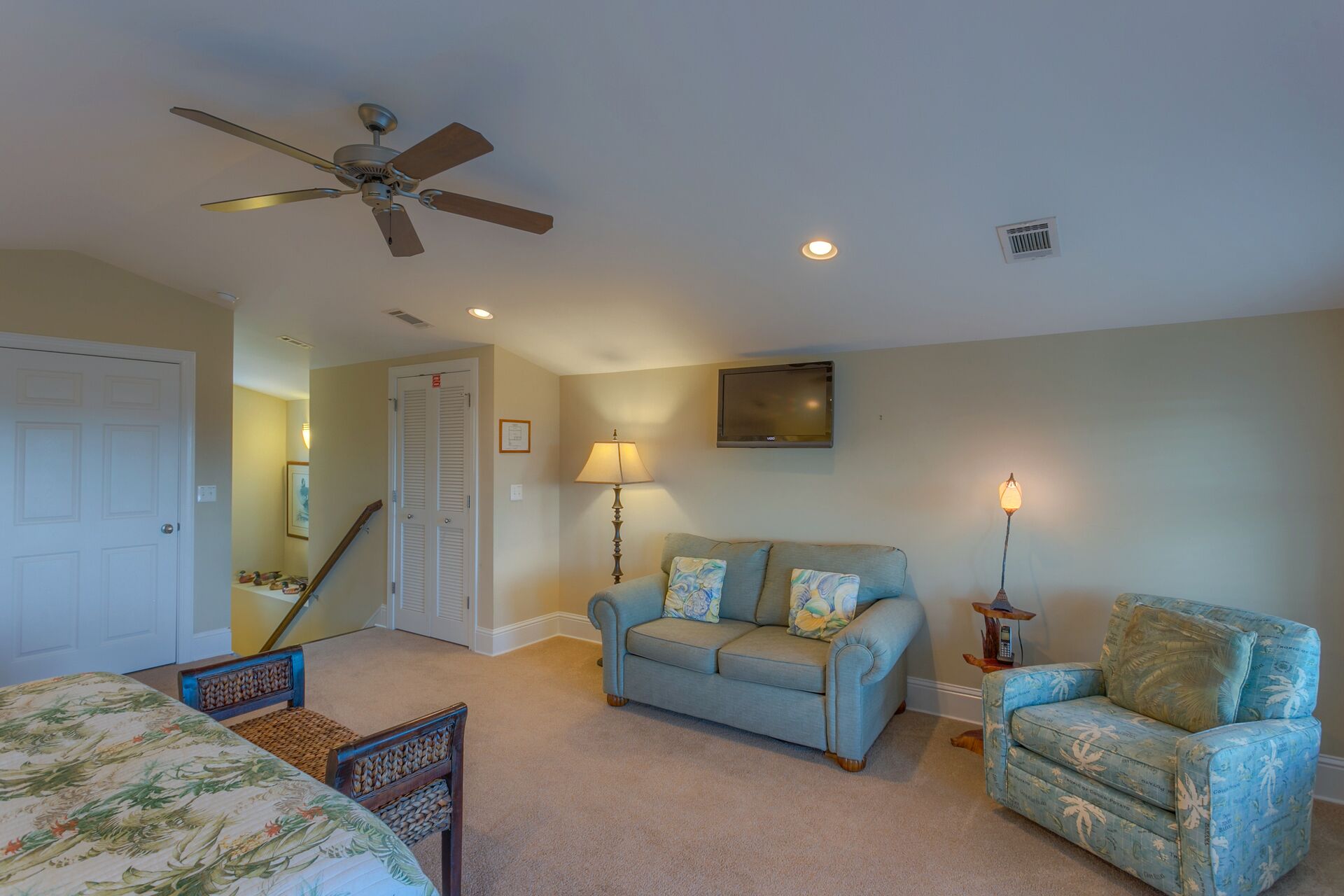 A bedroom with a bed, a ceiling fan, a sofa, a chair, a TV, and a lamp.