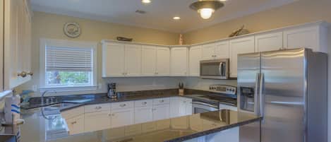A modern kitchen with white cabinets, stainless steel appliances, granite countertops, and pendant lighting.