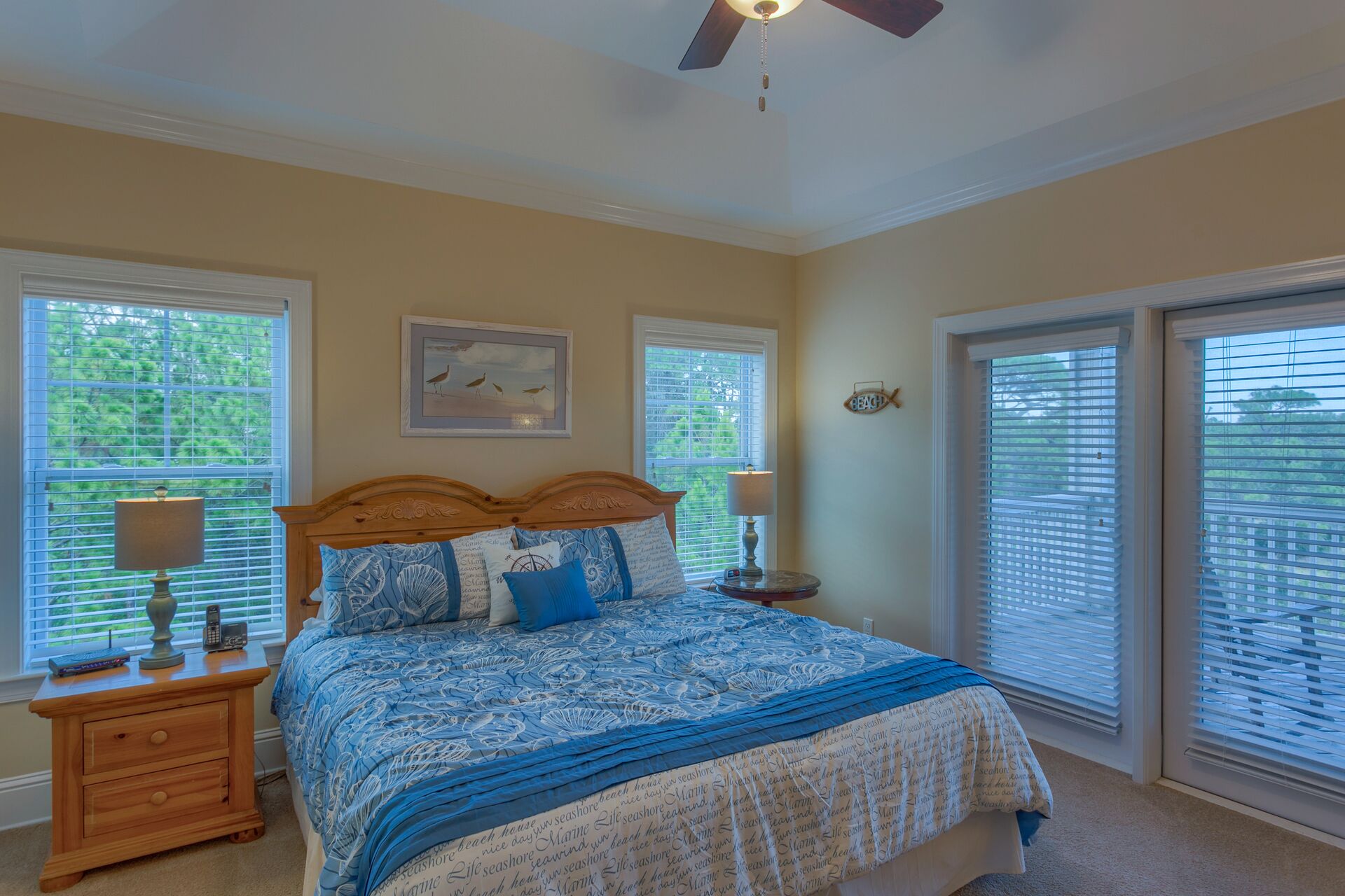 A bedroom with a bed, two bedside tables, a ceiling fan, and two windows with blinds.