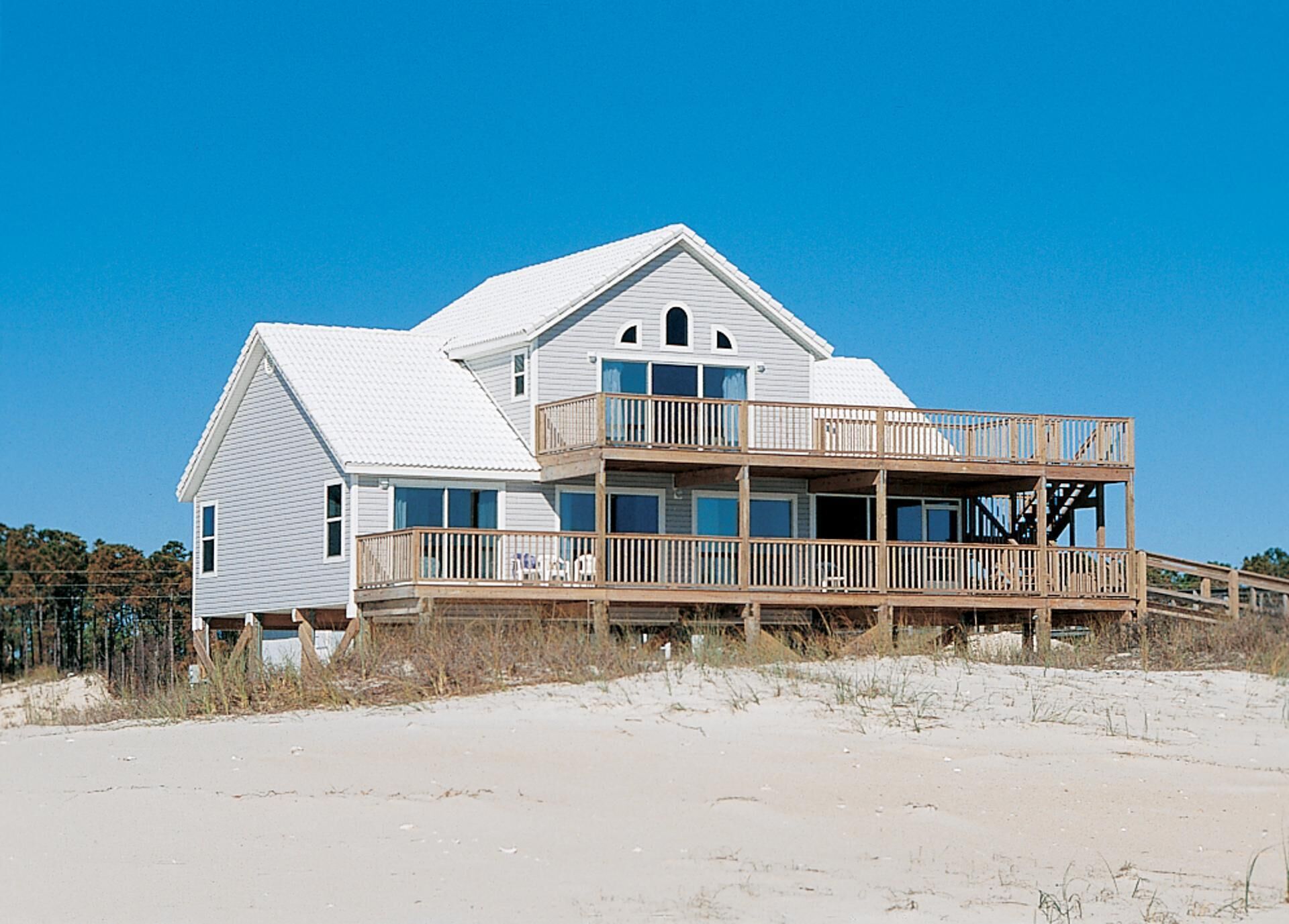 Une maison de plage à deux étages, dotée d’un balcon et d’un escalier menant à l’étage supérieur.