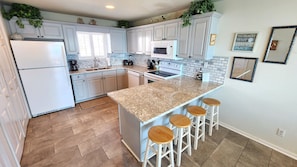 A modern kitchen with white cabinets, a granite countertop, and a central island with bar stools. - Beachfront with large sundecks! (St. George Island)