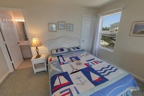 A bedroom with a bed, a nightstand, a lamp, a window with a view, and a door. - Beachfront with large sundecks! (St. George Island)