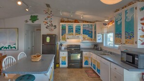 Una cocina con una isla central, armarios blancos decorados con motivos marinos, un refrigerador, estufa, microondas y un fregadero.