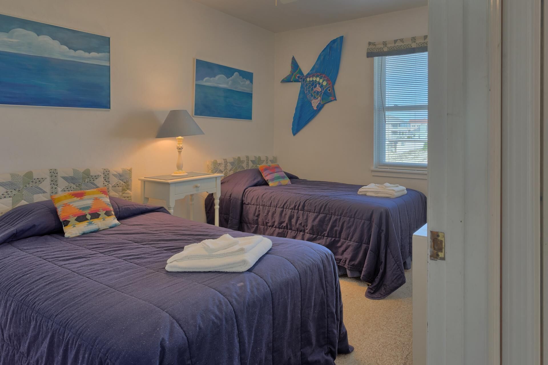A bedroom with two beds, a nightstand with a lamp, and artwork on the walls.