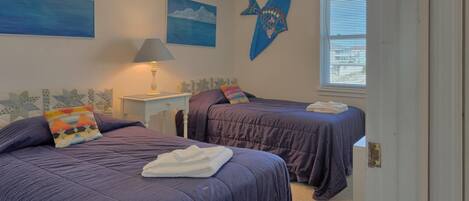 A bedroom with two beds, a nightstand with a lamp, and artwork on the walls.