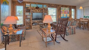 Una sala de estar acogedora con televisor, estanterías, una mecedora y un comedor.