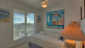 Un dormitorio con cama, ventilador de techo, lámpara y obras de arte en las paredes.