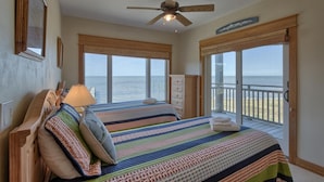 A bedroom with two beds, a ceiling fan, and large windows overlooking the ocean. - BAY FRONT WITH PRIVATE DOCK! HOT TUB! (St. George Island)