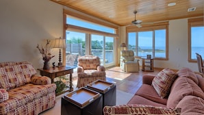 A spacious living room with a large window overlooking a body of water, wooden ceiling, and a variety of seating options. - BAY FRONT WITH PRIVATE DOCK! HOT TUB! (St. George Island)