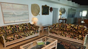 A living room with two floral-patterned sofas, a glass coffee table, and a patterned rug. - Sandy Beach: 3  BR, 3  BA House in St. George Island, Sleeps 8 (St. George Island)