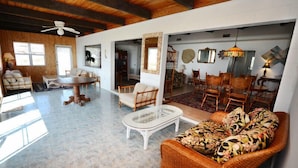 A spacious living area with a high ceiling, wooden beams, a dining area with wooden chairs, and a wicker sofa with a floral cushion. - Sandy Beach: 3  BR, 3  BA House in St. George Island, Sleeps 8 (St. George Island)